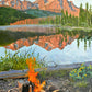 An oil painting depicting a morning scene with a coffee pot by a fire, Stanley Lake and the Sawtooth Mountains in the background.